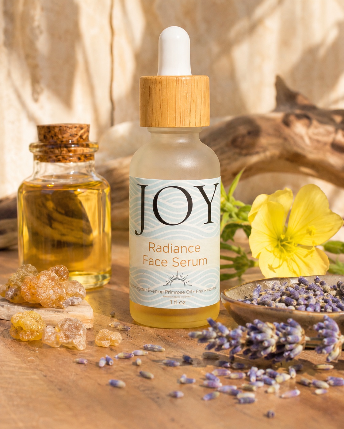 JOY Radiance Face Serum surrounded by frankincense, lavender, jojoba oil and evening primrose in warm light